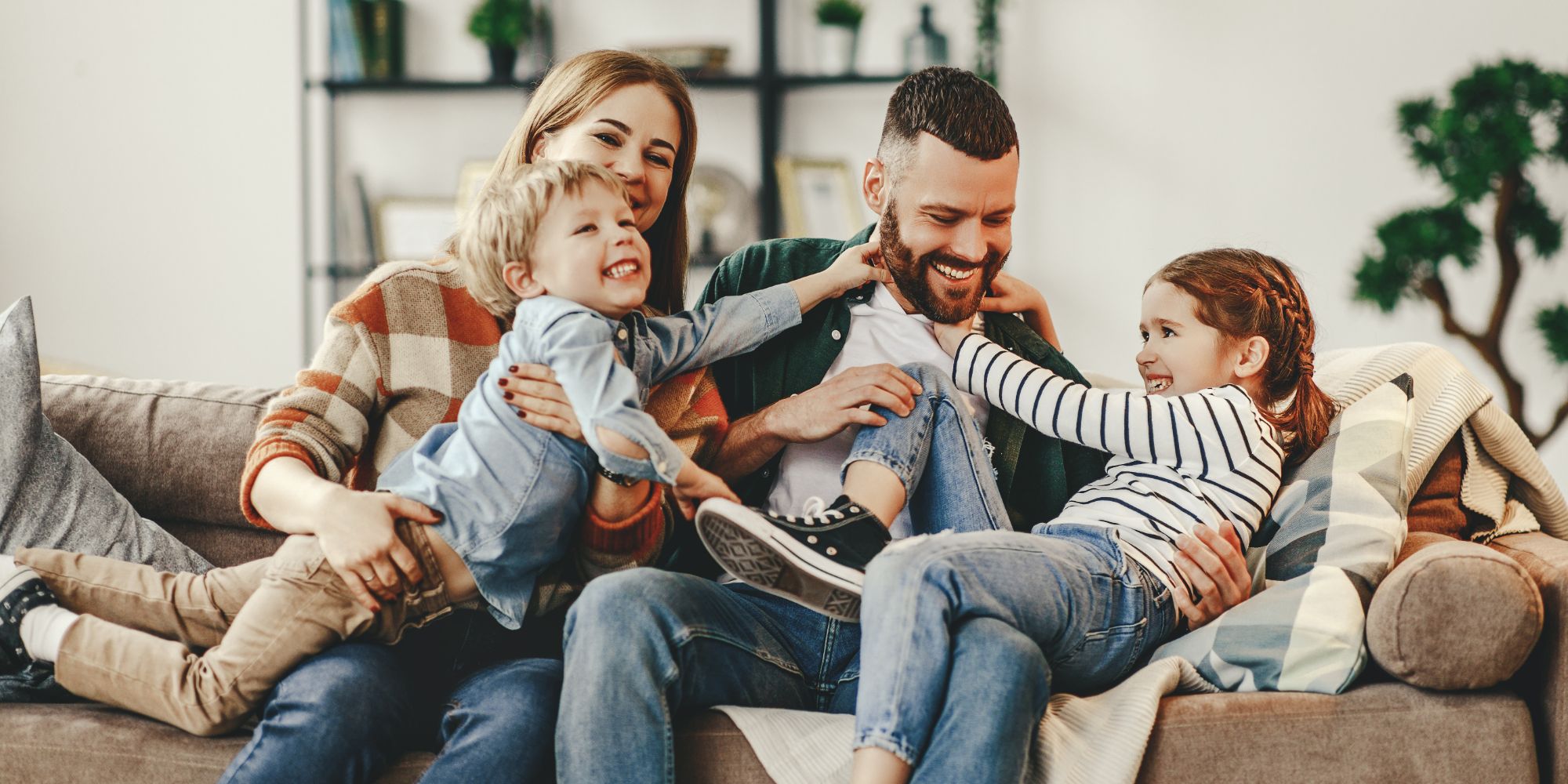 A mother, father, son and daughter laughing together on a sofa at home